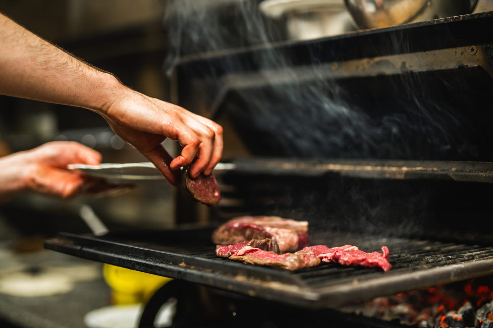 Hands turning steak on the grill with tongs